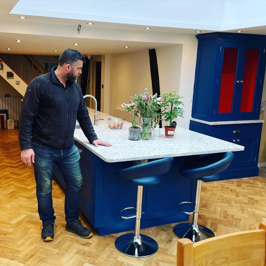 Jonathan Wilton, founder of Custom House Kitchens, standing at a hand-painted blue kitchen island